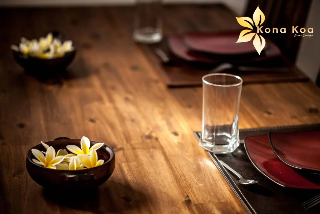 Wooden table in a bungalow at Kona Koa Eco Lodge, with a glass and frangipani flowers in a bowl.
