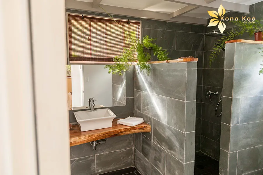 Bathroom entrance in a bungalow at Kona Koa Eco Lodge, with walk-in shower and basin on raw wood.