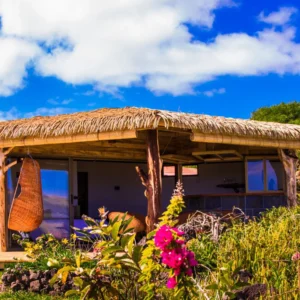 Open tropical Haka Nini bungalow on Rapa Nui with thatched roof, hanging wicker chair and bougainvillea.