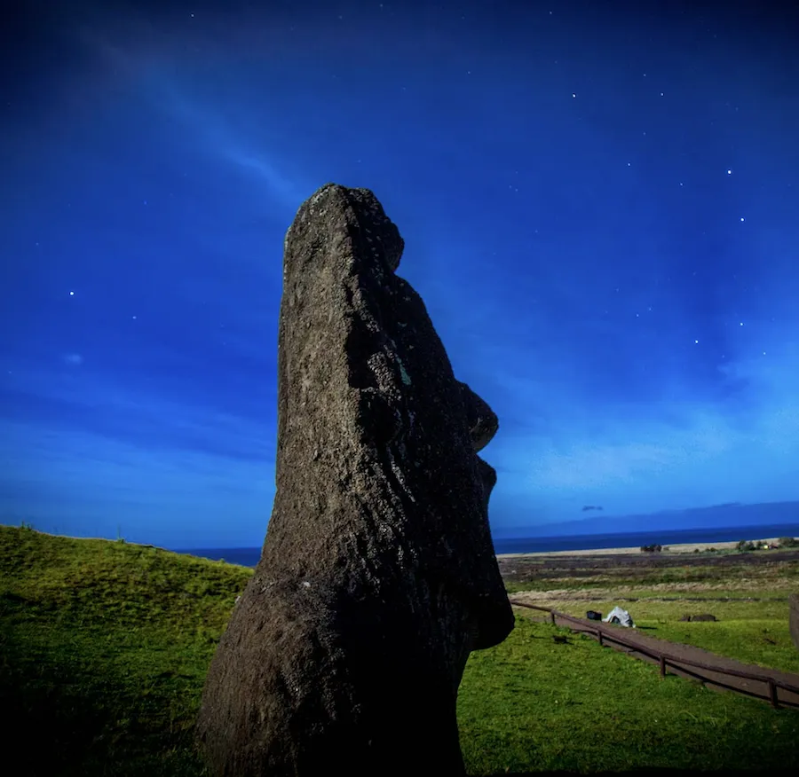 A lone moai on Rapa Nui against a starry night sky and the ocean.