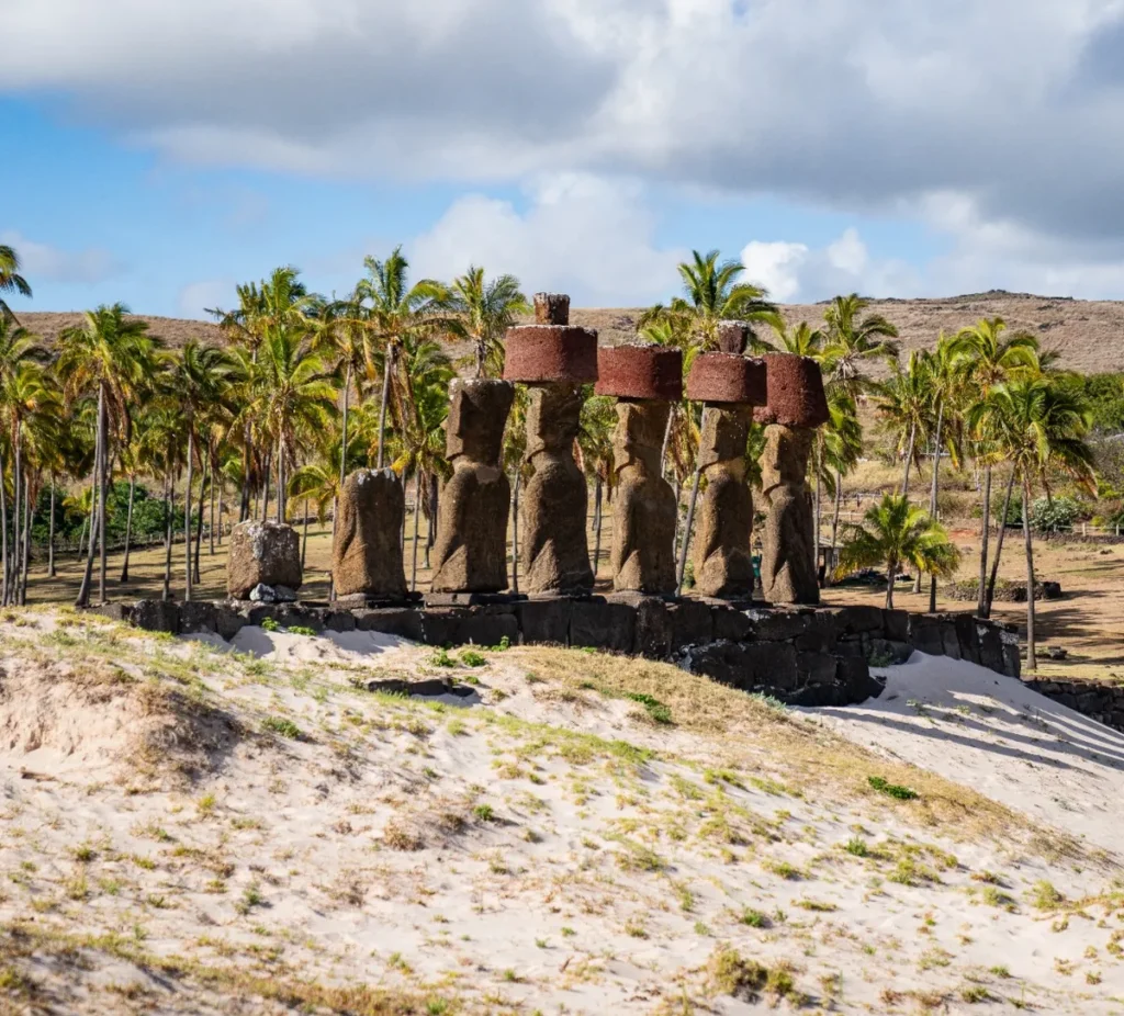 Ahu Nau Nau at Anakena, moai crowned with red pukao in front of a palm grove and the white sand of the beach.