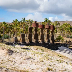 Ahu Nau Nau at Anakena, moai crowned with red pukao in front of a palm grove and the white sand of the beach.
