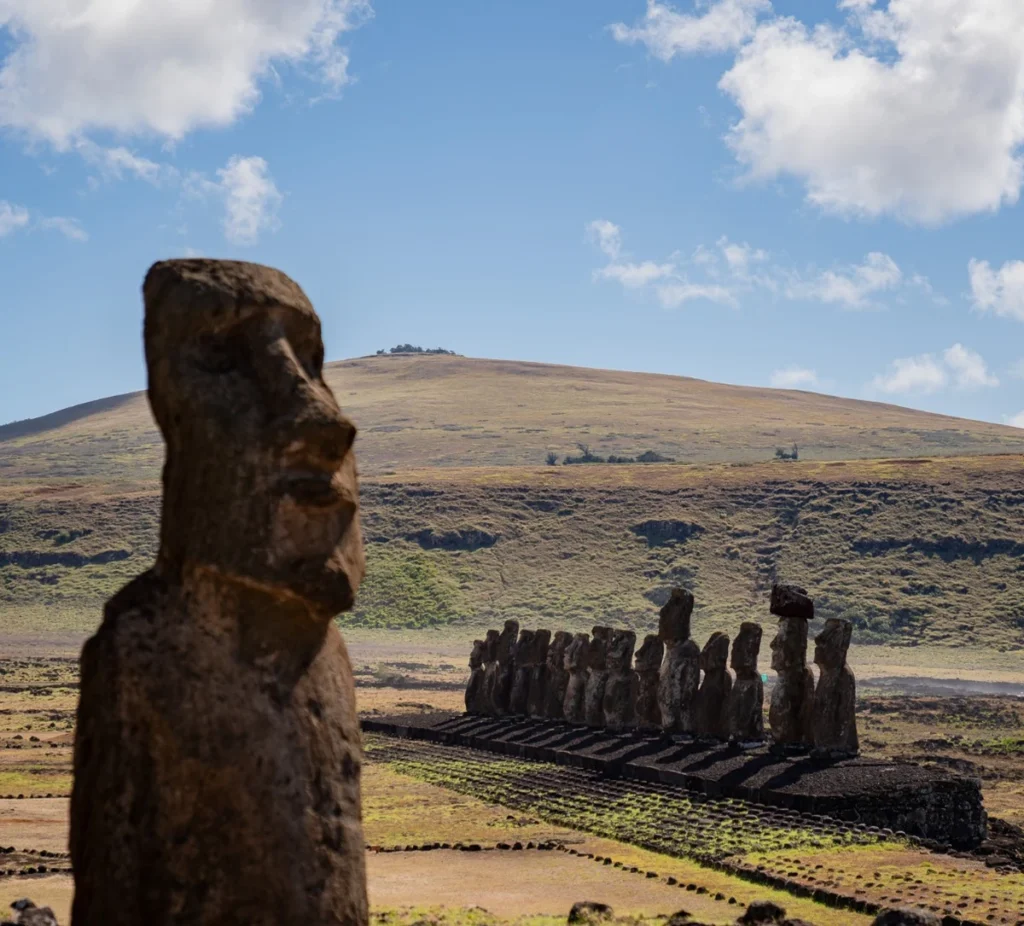 The fifteen moai of Ahu Tongariki on their platform, seen from the hillside, with a lone moai in the foreground.