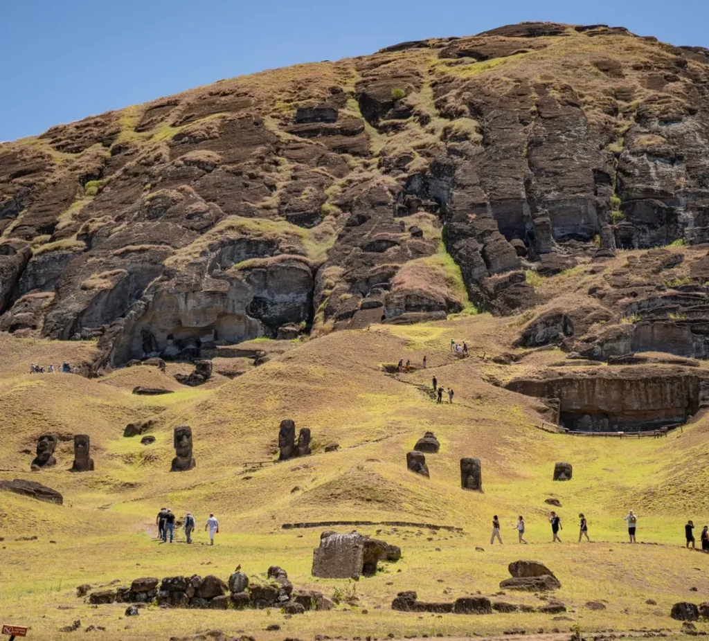 The slope of Rano Raraku covered with unfinished moai, visitors walking the path at the foot of the quarry.