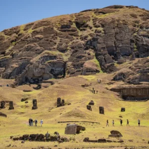 The slope of Rano Raraku covered with unfinished moai, visitors walking the path at the foot of the quarry.