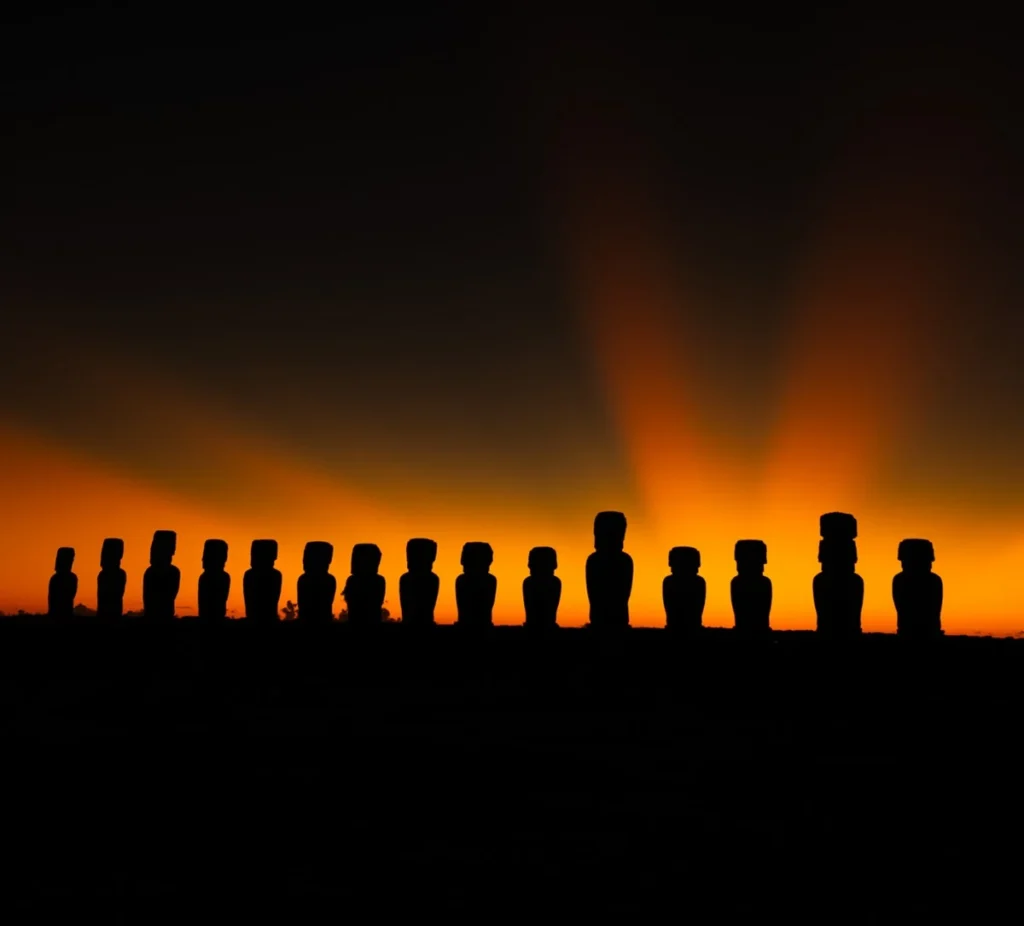 The fifteen moai of Ahu Tongariki silhouetted against an orange sky at sunrise.